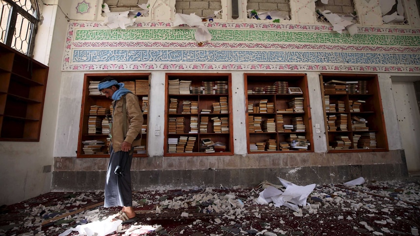 A Houthi militant looks at the damage after a suicide bomb attack