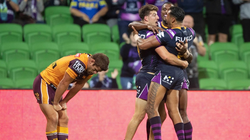 Curtis Scott hugs two Storm teammates as Andrew McCullough bends over to look at the ground in the foreground.