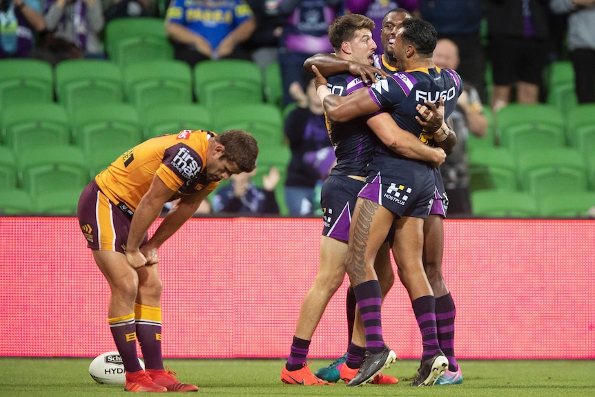 Curtis Scott hugs two Storm teammates as Andrew McCullough bends over to look at the ground in the foreground.