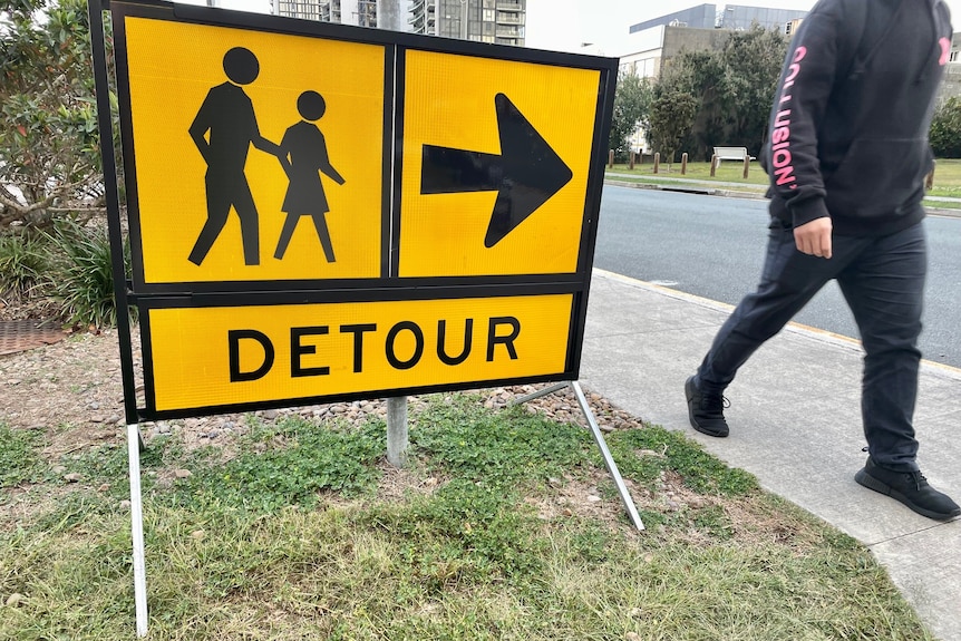 Yellow sign that says 'closed to pedestrians' with a person walking past.