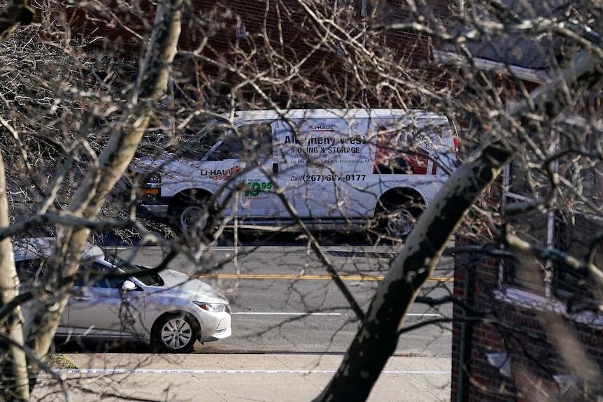 A photo taken with a tele lens shows a white van emblazoned with promotional text in a car park