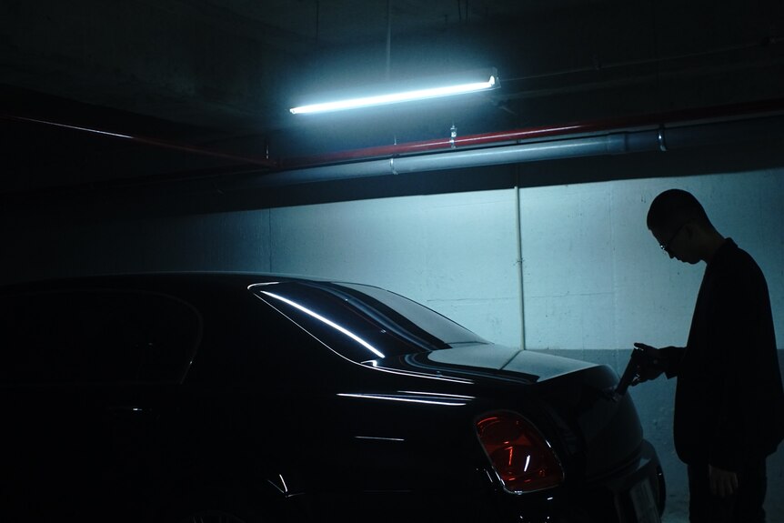L'ombre d'une personne debout à côté d'une voiture à l'intérieur d'un parking avec un néon bleu 