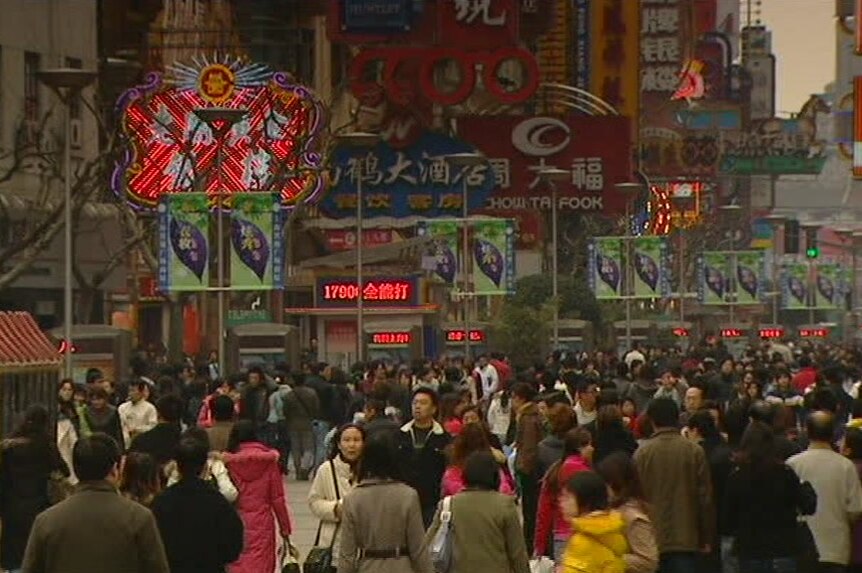 Pedestrians walk down street and past shops on busy street in China.