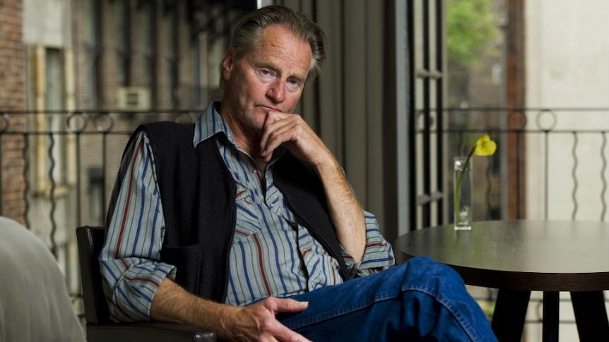 Sam Shepard sits, legs crossed, on a porch.
