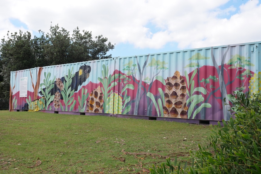 A shipping container covered in murals of birds and flowers