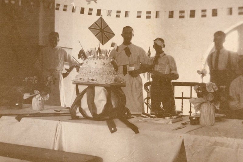 A sepia photo of patients with large cake and bunting