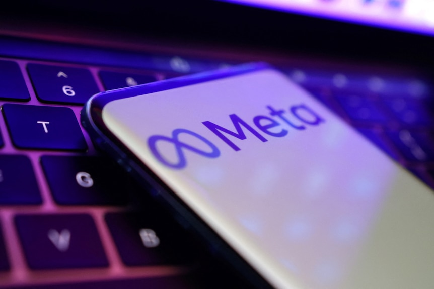 A phone displaying the meta logo sits on a computer keyboard