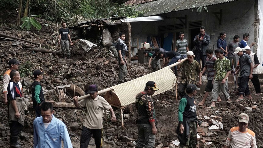 Rescue workers carrying a body on a covered stretcher at the site of a landslide.