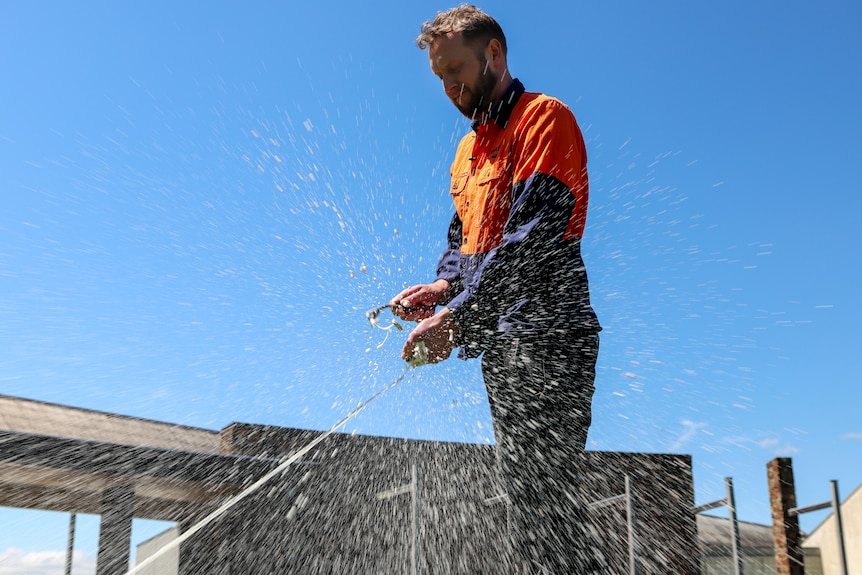 Sparkling wine spurts out of a bottle opened by a man in orange and blue vest