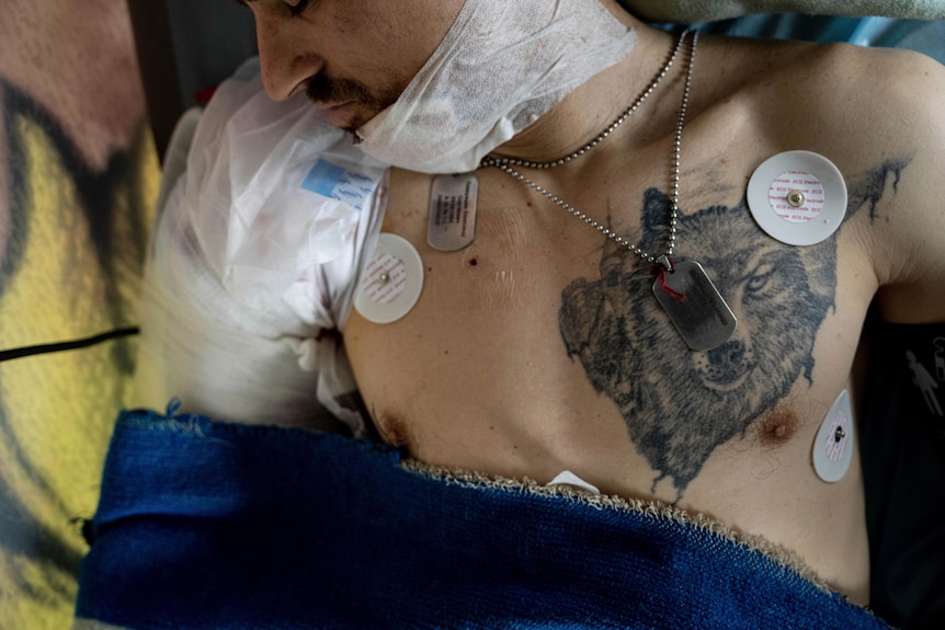 A man has bandages on his arm and neck and a large tattoo on his chest. 