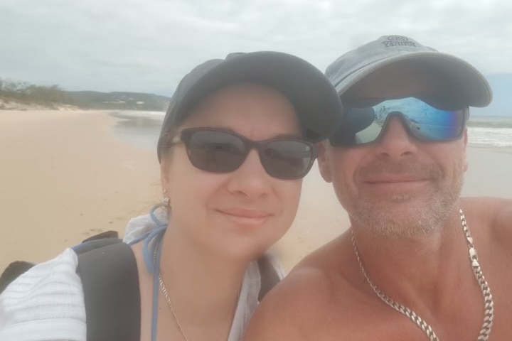 woman and man in sunglasses standing on beach smiling with sand in background