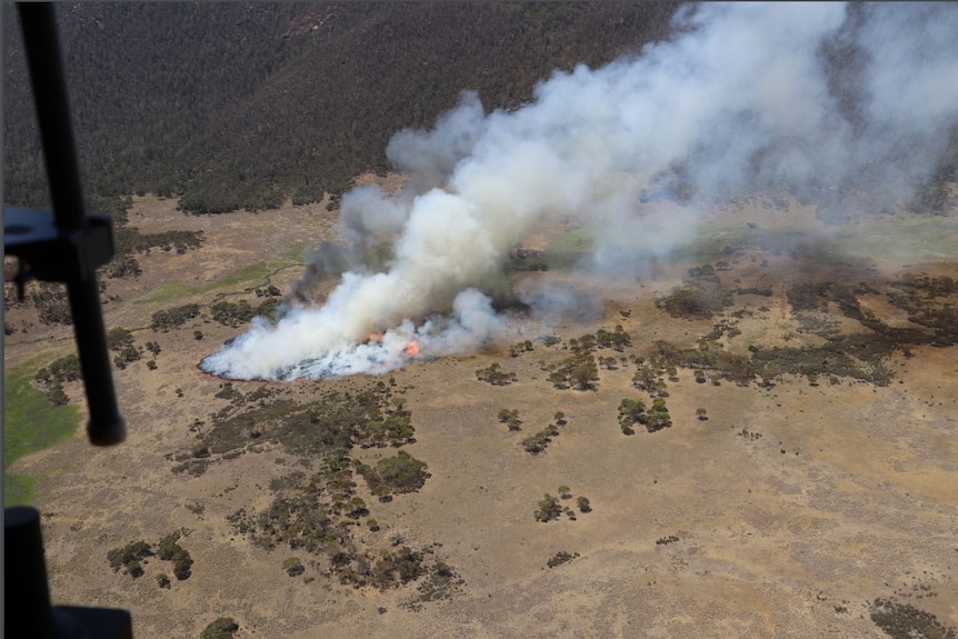 An aerial photograph from within a helicopter shows a patch of fire spreading through bushland.