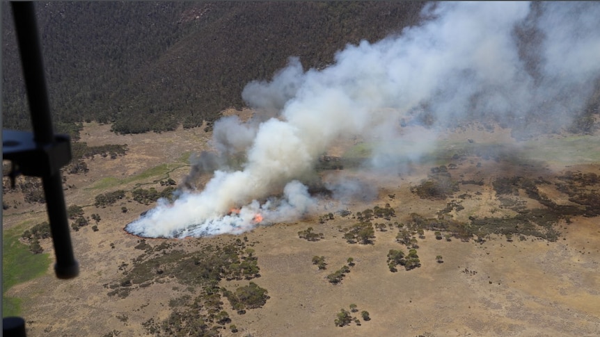 An aerial photograph from within a helicopter shows a patch of fire spreading through bushland.