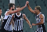 Port Adelaide players celebrate with high-fives wearing the black and white stripped, prison bar jersey