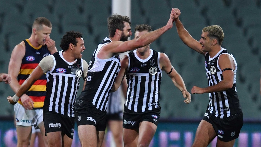 Port Adelaide players celebrate with high-fives wearing the black and white stripped, prison bar jersey