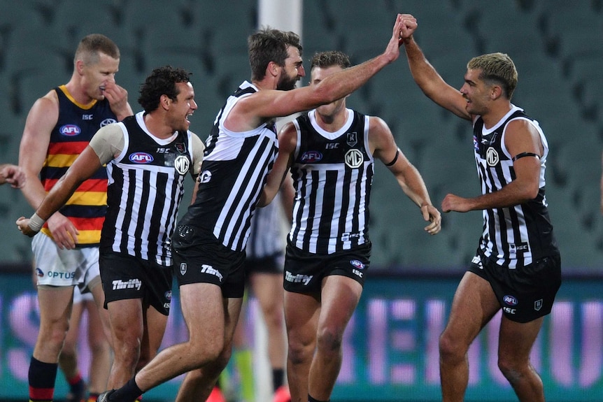 Port Adelaide players celebrate with high-fives wearing the black and white stripped, prison bar jersey