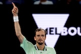 Tennis player Daniil Medvedev points a finger to the sky in front of a "Melbourne" sign at the Australian Open.
