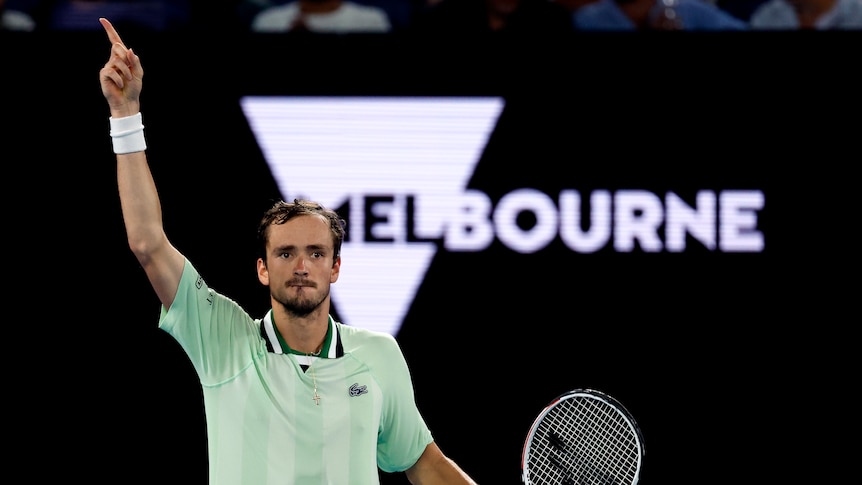 Tennis player Daniil Medvedev points a finger to the sky in front of a "Melbourne" sign at the Australian Open.