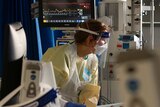 A nurse is seem through a mess of medical equipment and wires as she works with a patient inside the Intensive Care Unit.