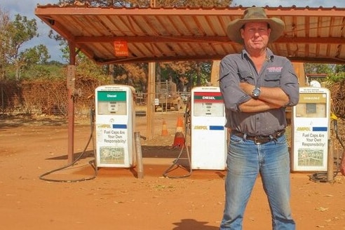 A man stands in front of a petrol station. 