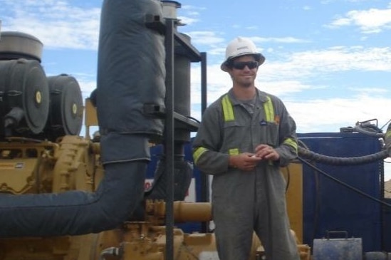 Cameron in his work clothes and hard hat standing on a rig