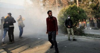 A man, standing in a cloud of smoke in the street, yells.