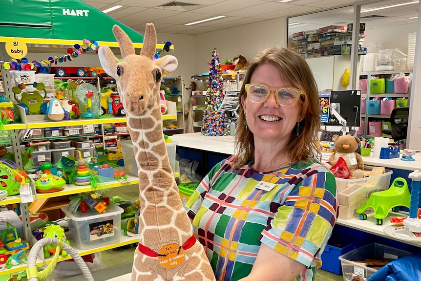 A woman in a colourful top smiling with a toy giraffe in her arms.