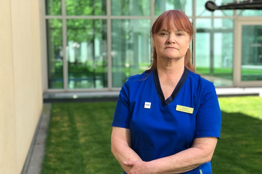 A woman in a blue nurse's uniform stands in front of a building