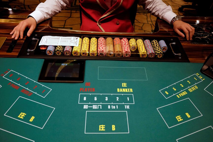 A casino employee sitting with a stack of chips at a gambling table.