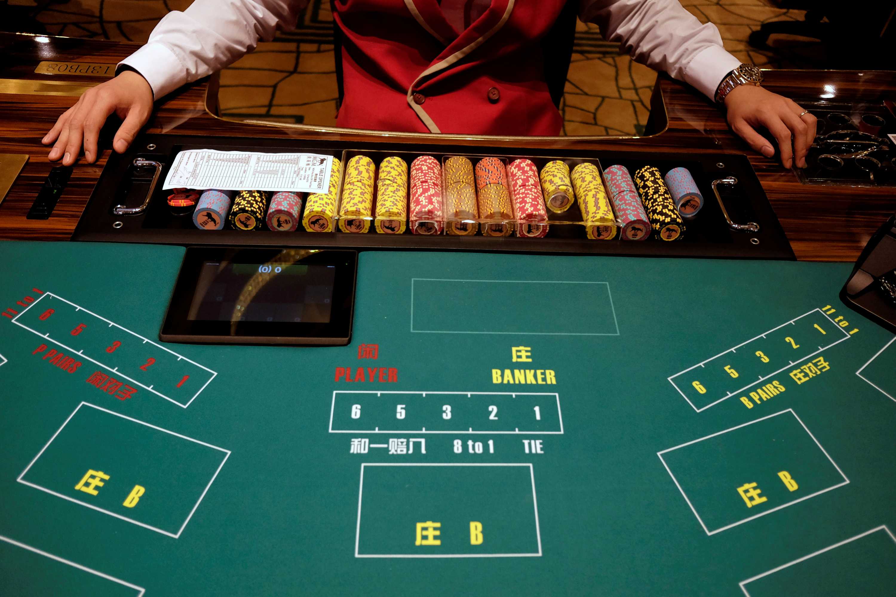 A casino employee sitting with a stack of chips at a gambling table.