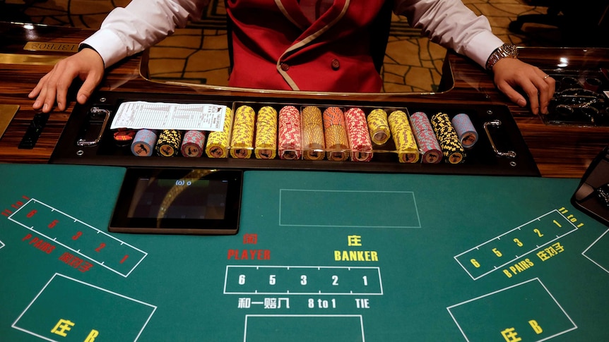 A casino employee sitting with a stack of chips at a gambling table.