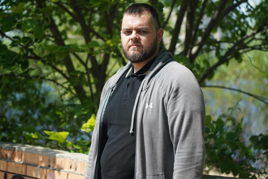 Man in a black shirt and grey hoodie standing outside.
