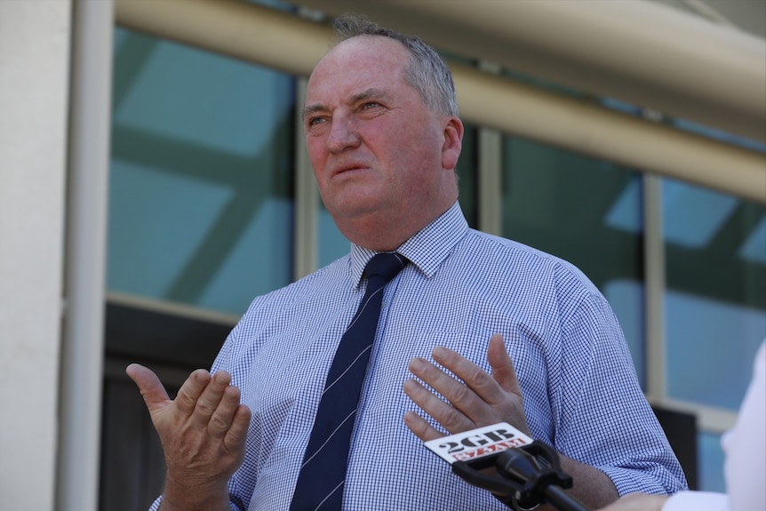 Barnaby Joyce in a shirt and a dark tie looks to the left of camera with his lips pursed and his palms facing upwards