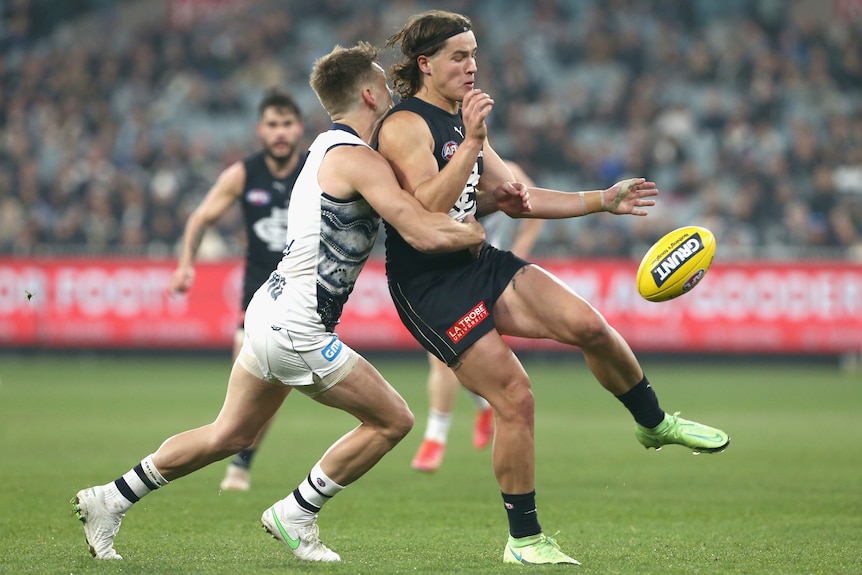 A Carlton AFL player is tackled by a Geelong opponent as he kicks the ball.