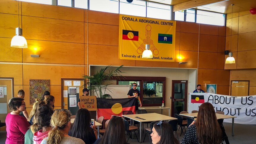 Students inside UNE's Oorala Centre with a protest banner that says About us Without Us.