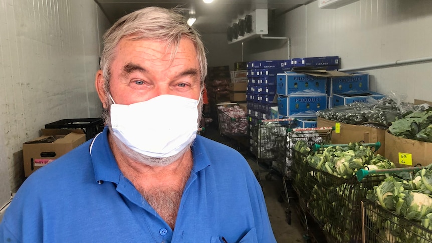 A man wearing a mask, with a cold room behind behind him filled with boxes and cauliflowers.