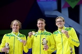 australian swimmers stand together on a podium holding medals all wearing matching yellow jackets