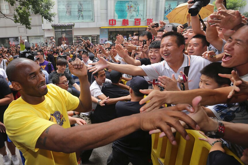 Kobe Bryant reaches over a barricade to shake hands with some excited Chinese fans. The crowd is massive.