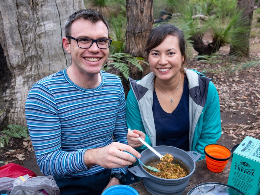 A couple eat camp food together in the bush.