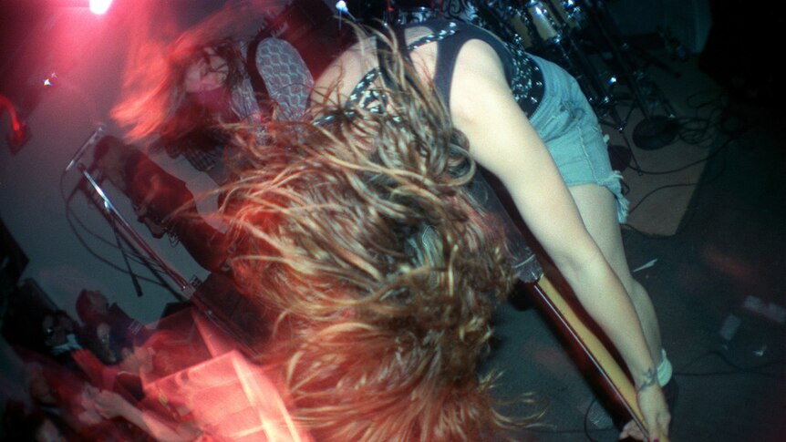 Woman dramatically playing guitar bent forward, hair hanging forward, crowd in front