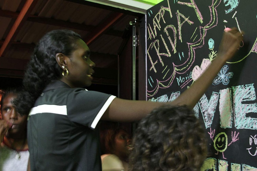 a woman writes on a blackboard with children around her