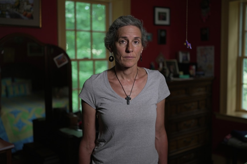 A woman in a grey shirt looking sombre.