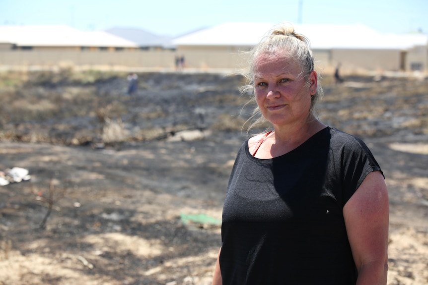 A woman stands next to a charred patch of earth.
