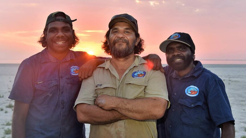 Three rangers photographed with the sun setting in the background.