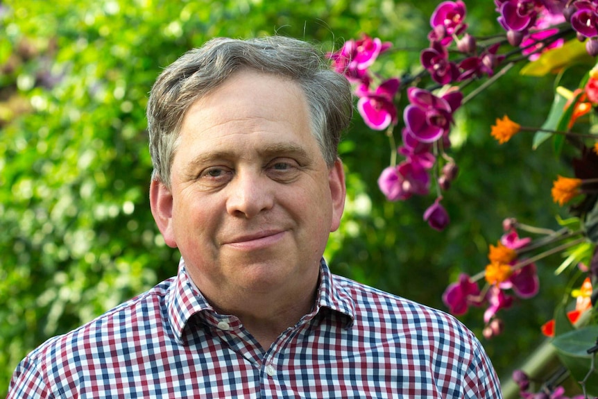 Man stands in front of flowers including orchids.