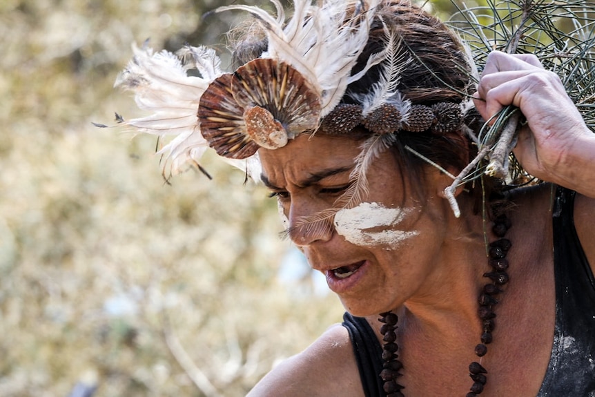 Close up of woman in traditional Indigenous headdress and face painted in ochre, dancing