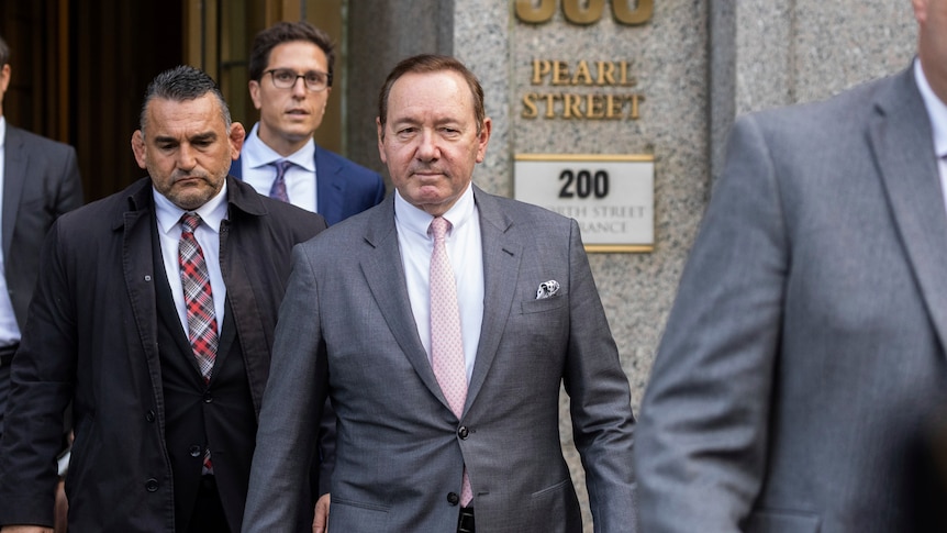 kevin spacey (center) wears a grey suit as he walks out of a court room