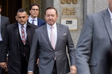 kevin spacey (center) wears a grey suit as he walks out of a court room