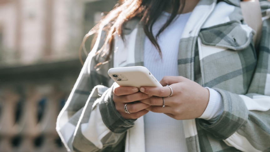 Image of a woman wearing a grey and white checked coat and white shirt holding a phone