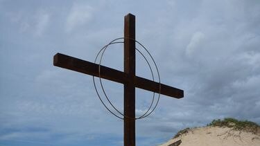 A large Christian cross mounted with a propeller stands on a monument in the sand.